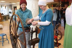 Luceta showing a museum patron how to spin fiber on a wheel.